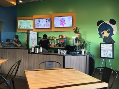 A colorful café interior with a green wall, digital menus, and a cartoon character mural. Staff are preparing drinks.